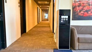 A hotel hallway with carpeted floors, a water dispenser, a sofa, and a painting on the wall. - Seeds Hotel Premier One City Subang (Subang Jaya)