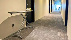 A hallway with carpeted flooring, a metal ironing board, and a door with a black frame. - Seeds Hotel Premier One City Subang (Subang Jaya)