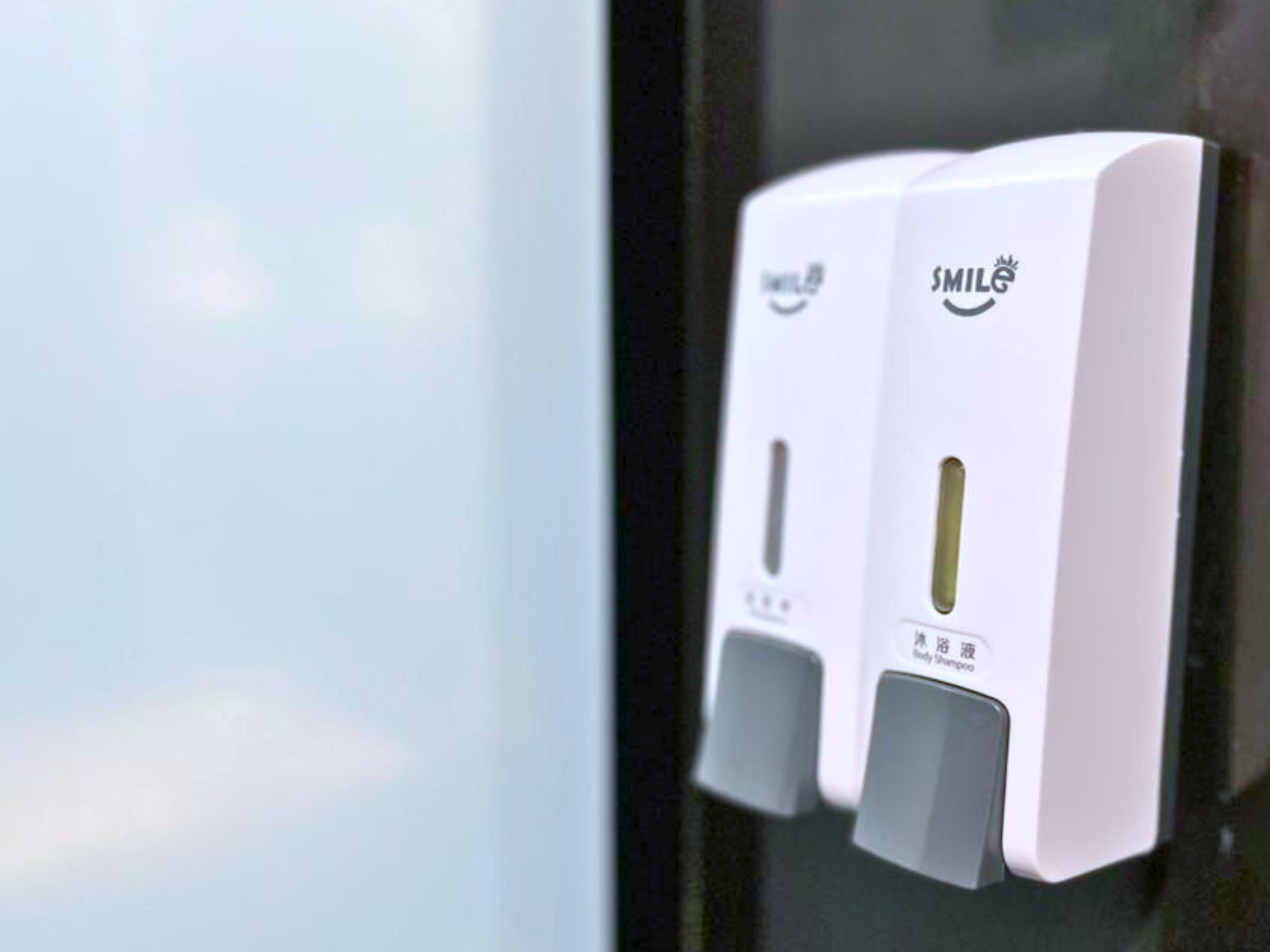 Two white hand sanitizer dispensers mounted on a glass wall.