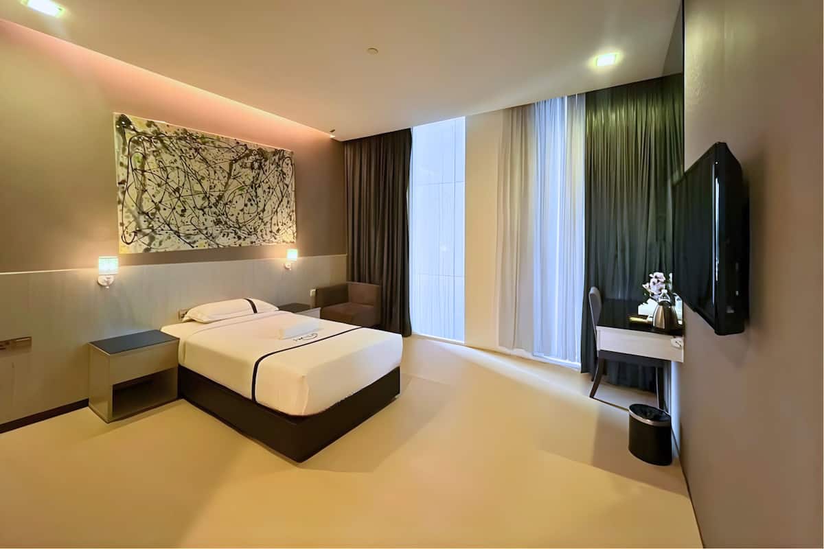 Een moderne hotelkamer met een bed, nachtkastjes, een flatscreen televisie, een bureau met stoel en een groot raam met gordijnen.