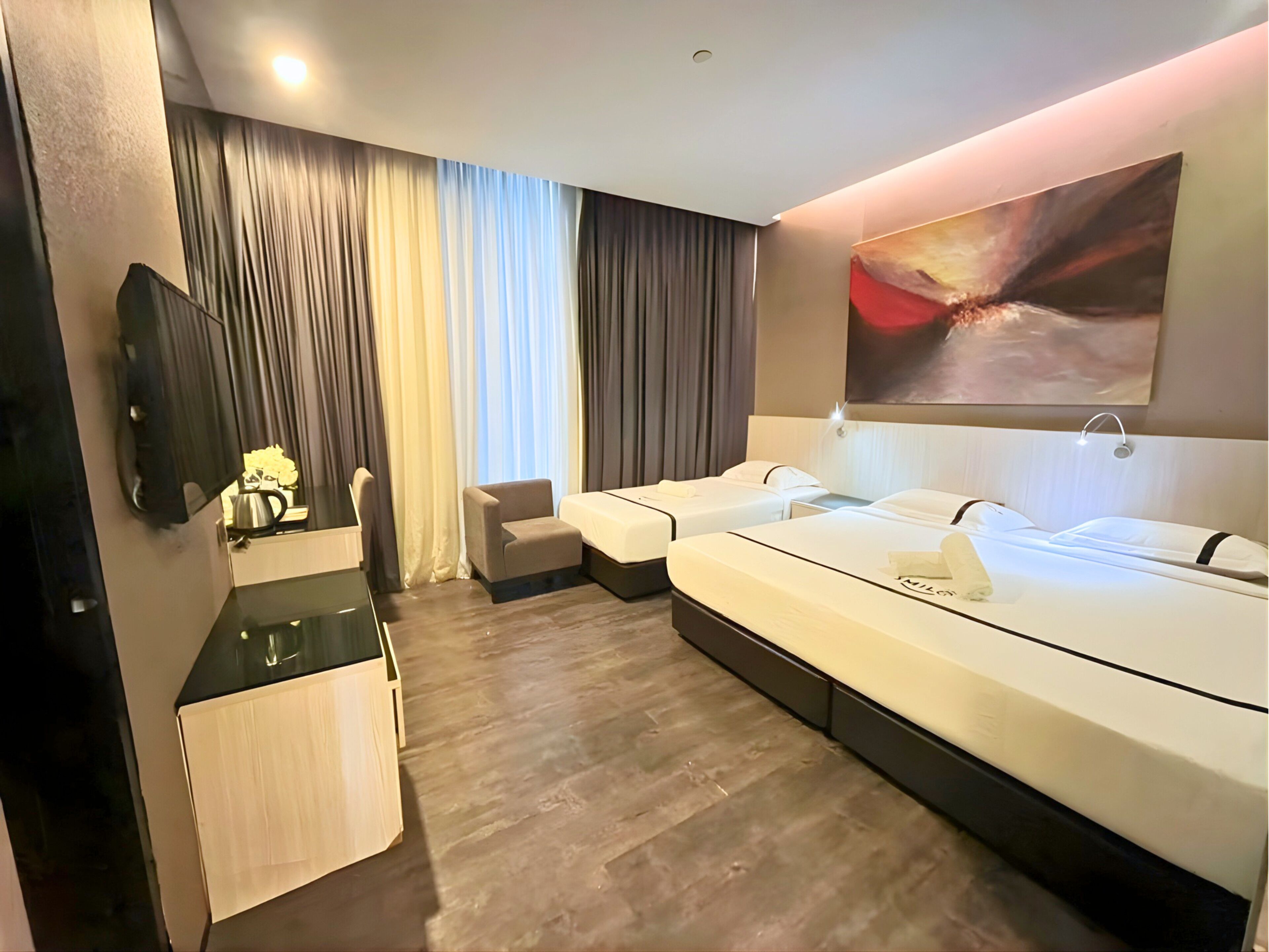 Une chambre d’hôtel avec deux lits, un bureau, une chaise, une télévision et un tableau au mur.