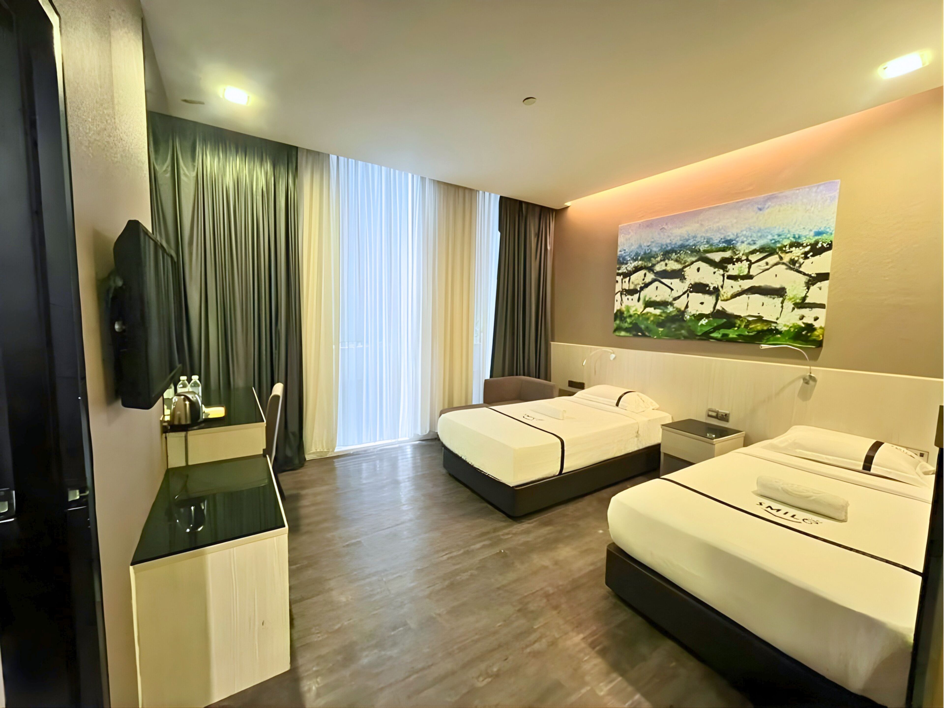 Habitación de hotel con dos camas, un escritorio, una silla, un televisor y un cuadro en la pared.