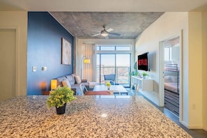 A modern living room with a large granite island, a ceiling fan, and a TV mounted on the wall. - DT PHX 2BR Retreat | Balcony, Pool, Parking, W/D (Phoenix)