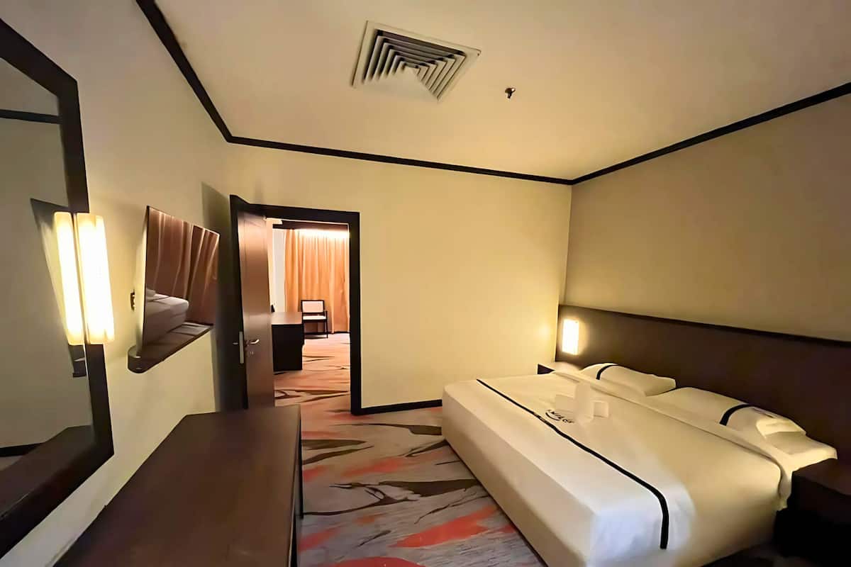 Ein Hotelzimmer mit Bett, Nachttisch und Spiegel. Eine Tür führt in einen weiteren Raum.