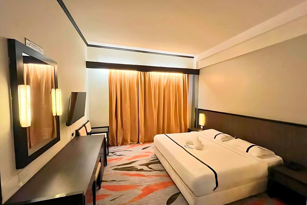 Ein Hotelzimmer mit Bett, Schreibtisch, Stuhl, Fernseher und einem fensterbepflanzten Fenster.
