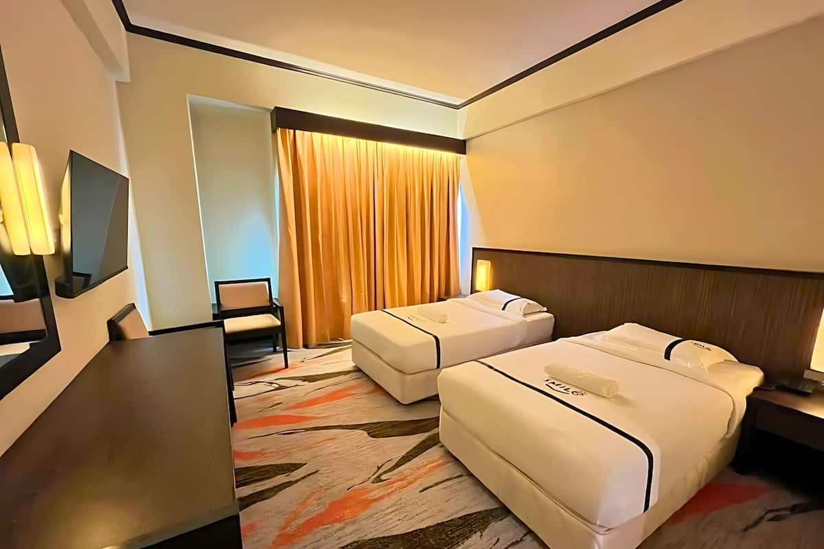 Ein Hotelzimmer mit zwei Betten, einem Schreibtisch, einem Stuhl und einem großen Fenster mit Vorhängen.