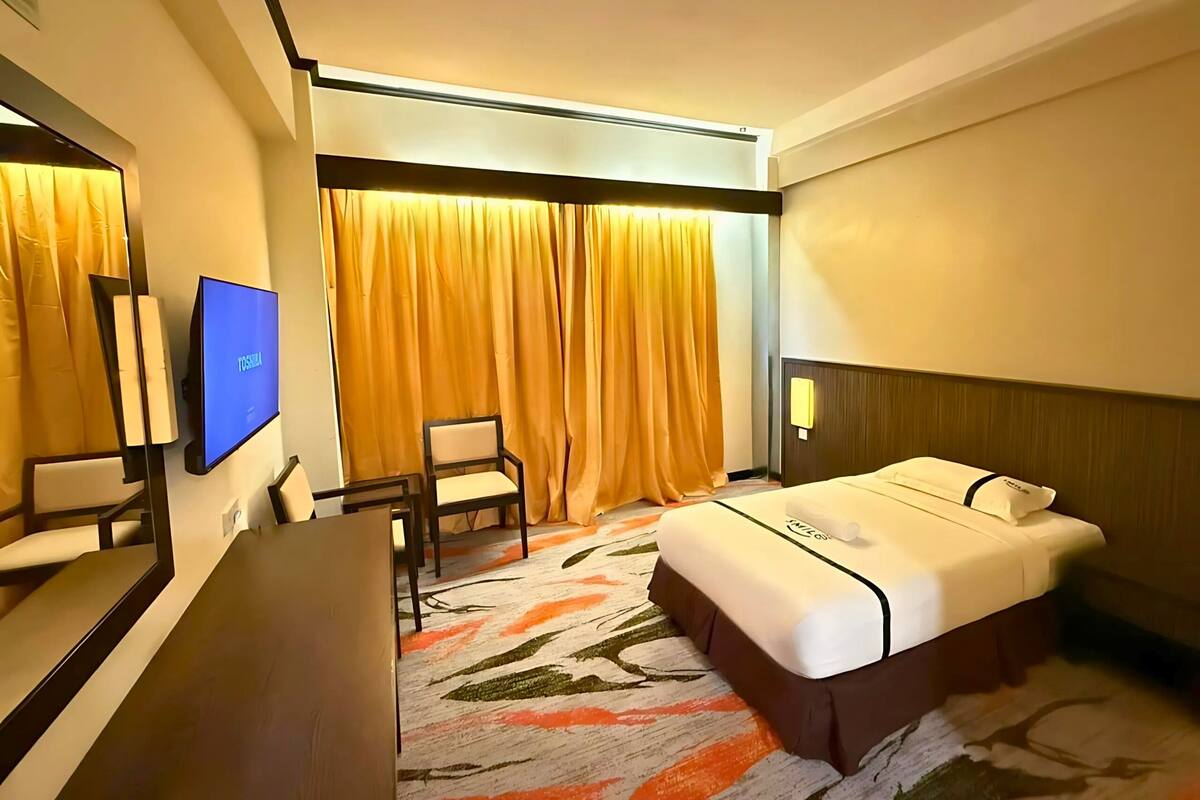 Ein Hotelzimmer mit einem Bett, einem Schreibtisch, einem Stuhl, einem Fernseher und einem Vorhang.
