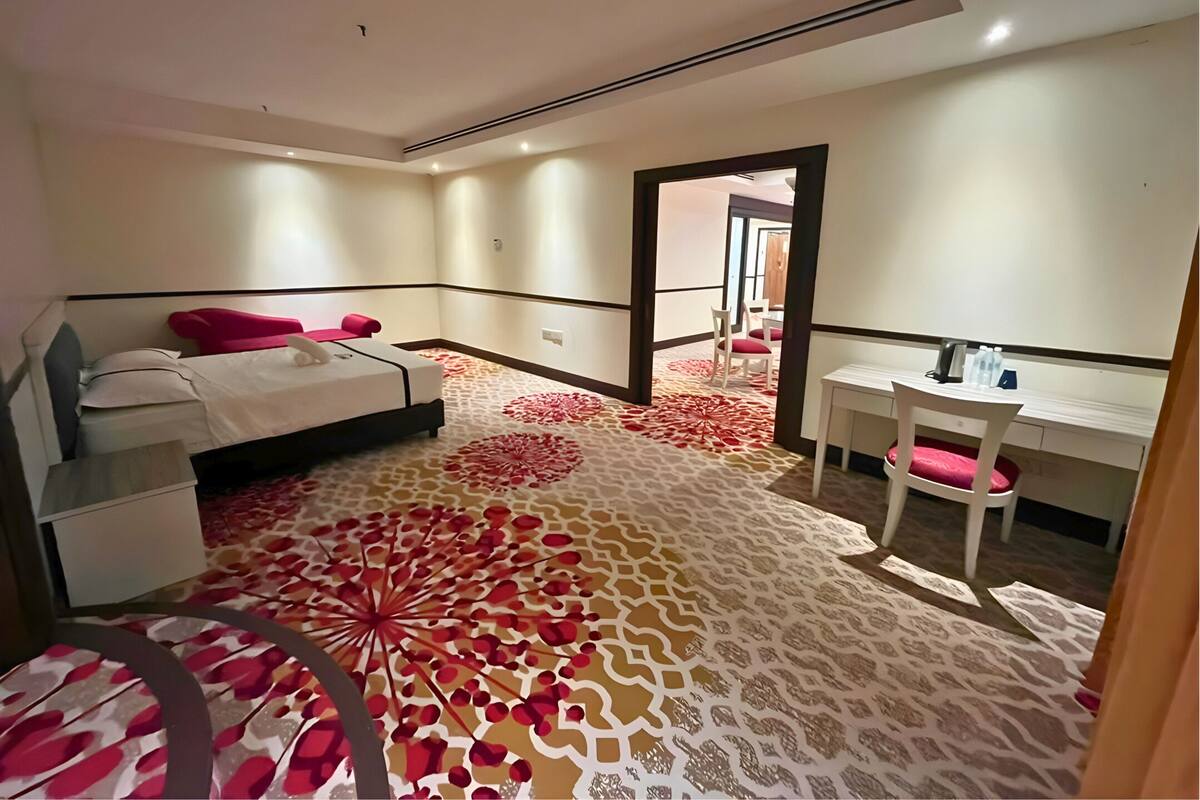 Ein Hotelzimmer mit Bett, Nachttisch, Schreibtisch, Stuhl und einem gemusterten Teppich.