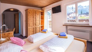 A hotel room with two beds, wooden cabinets, a desk with a lamp, and a TV on the wall. - Chalamandrin Hotel und Restaurant (Scuol)