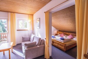 Una habitación con techo de madera, una cama con almohadas, un sofá, una mesa y una ventana con cortinas.