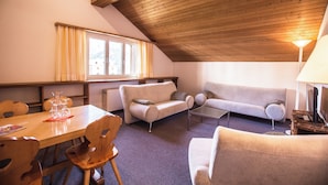 A cozy living room with a wooden ceiling, a sofa, a coffee table, and a dining table with chairs. - Chalamandrin Hotel und Restaurant (Scuol)