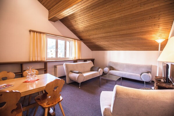 Una sala de estar acogedora con techo de madera, un sofá, una mesa de centro y una mesa de comedor con sillas.