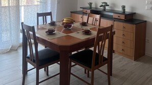 Un coin repas avec une table et des chaises en bois, un saladier de fruits, et un espace cuisine avec des placards et un plan de travail.