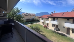 Un balcon donnant sur une cour, des bâtiments aux toits recouverts de tuiles rouges et des montagnes en arrière-plan.