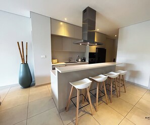 A modern kitchen with a central island, bar stools, and a large vase with bamboo sticks.