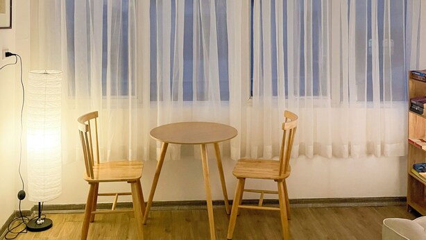 A room with a round table and two chairs, a large window with sheer curtains, a hanging light fixture, and a floor lamp. - Cozy studio with washing machine & dryer in the heart of Hà Nội (Hà Nội)