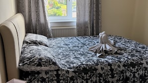 Une chambre à coucher avec un lit, une table de chevet, une lampe et une fenêtre avec des rideaux.