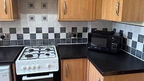 Une cuisine compacte avec des meubles en bois, une cuisinière à gaz, un four à micro-ondes et un petit réfrigérateur.