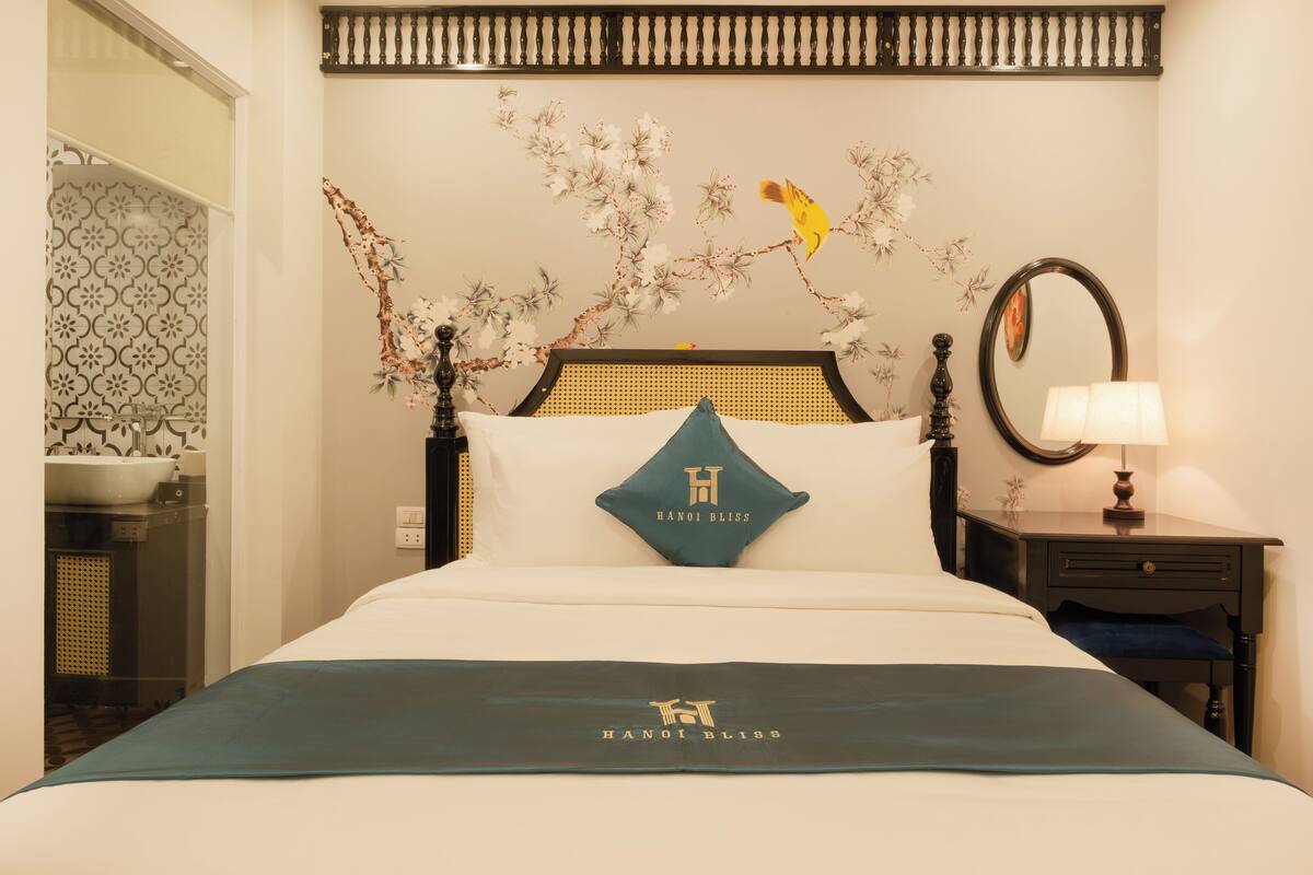 Une chambre d’hôtel avec un lit, une table de chevet, un miroir et un mur orné d’une fresque florale.