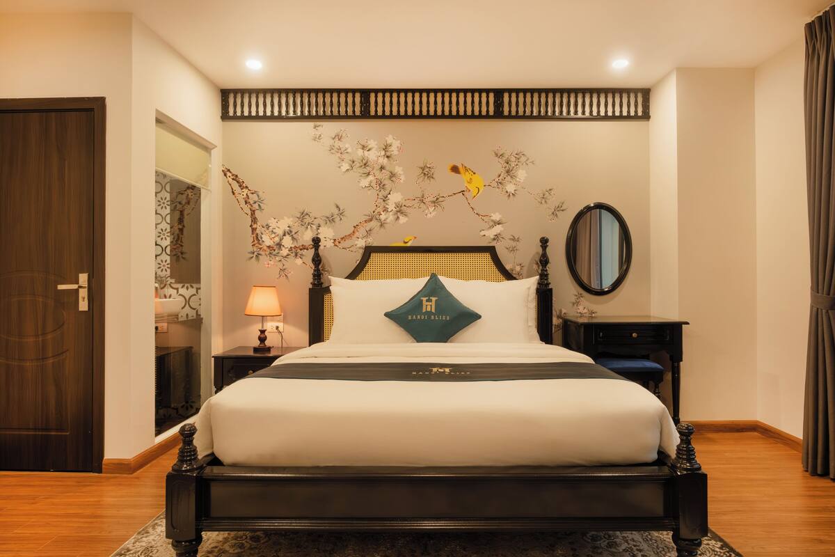 Une chambre à coucher bien rangée, avec un lit, une table de chevet, un miroir et une fresque murale.