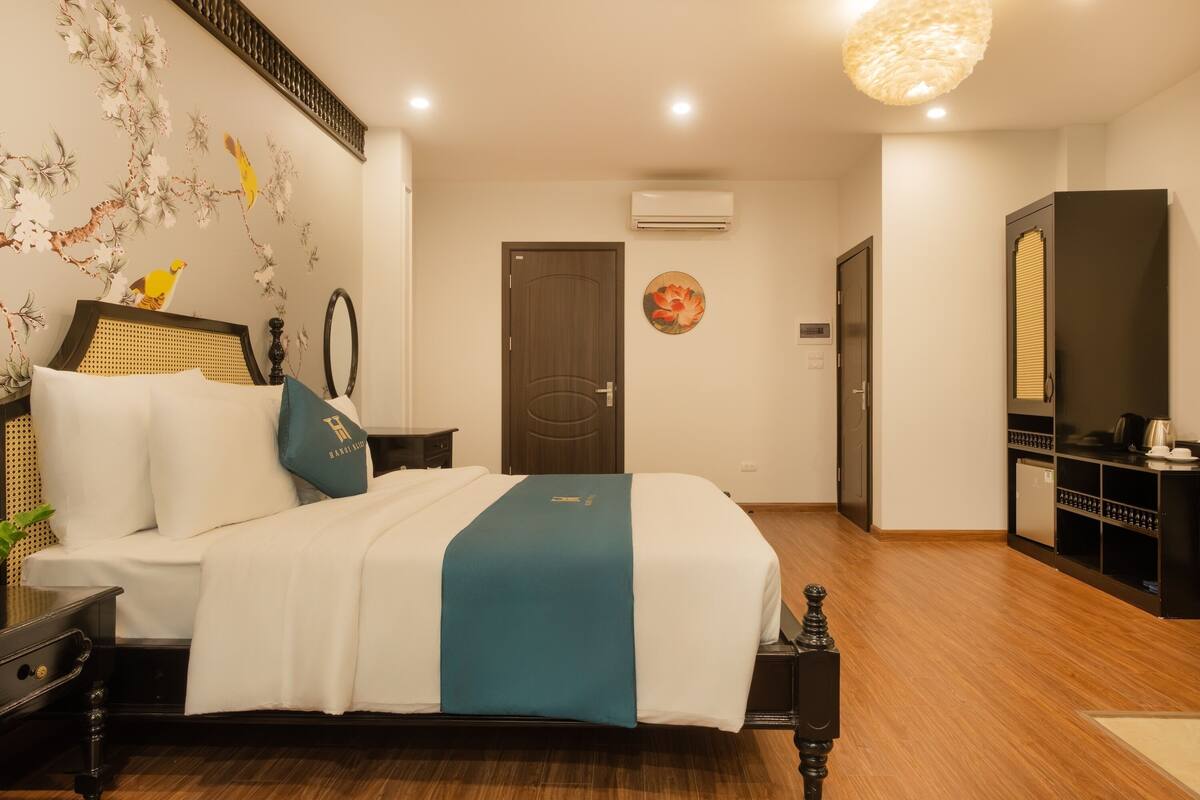 Une chambre d’hôtel avec un lit, une commode, un miroir et un mur recouvert d’un papier peint à motifs floraux.