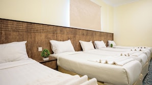 A hotel room with four beds arranged in a row, wooden headboard, and a small plant on the nightstand. - Saif Plus 3 (Makkah)