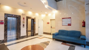 A lobby with an elevator, a blue sofa, and a fire extinguisher. - Saif Plus 3 (Makkah)