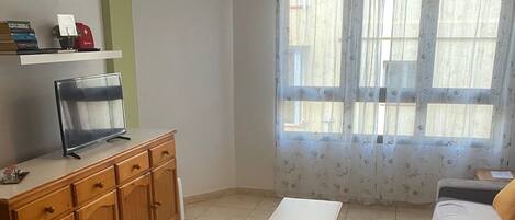 Una sala de estar con un aparador de madera, una mesita, un sofá y una ventana con cortinas florales.