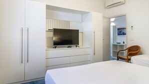 A bedroom with a bed, a television on a stand, a wardrobe, a chair, and an air conditioning unit. - Residence I Mari (Castiglione della Pescaia)