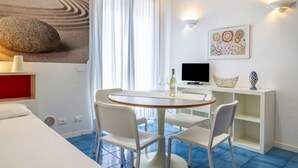 A modern room with a round table, white chairs, a TV, and artwork on the wall. - Residence I Mari (Castiglione della Pescaia)