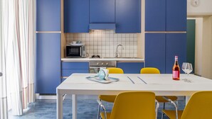 A modern kitchen with blue cabinets, a white countertop, and a dining area with yellow chairs. - Residence I Mari (Castiglione della Pescaia)