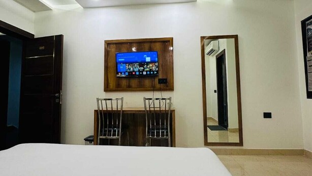 Een hotelkamer met een bed, een bureau met twee stoelen, een flatscreen televisie aan de muur, een plafondventilator en een spiegel.