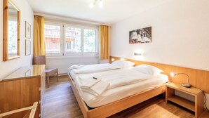 Een hotelkamer met twee bedden, een houten dressoir, een bureau, een stoel, een bureaulamp en een schilderij aan de muur.