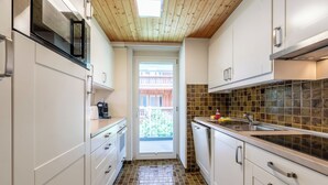 Een smalle keuken met witte kasten, een betegelde spatwand en een houten plafond.