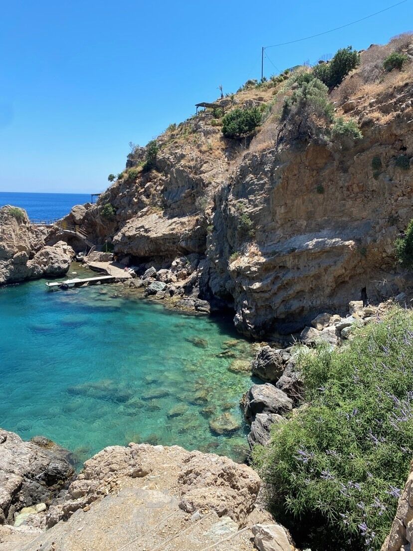 A rocky coastal landscape with clear water, a small dock, and a structure on the cliff.