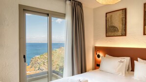 A hotel room with a bed, a nightstand, a lamp, a painting, and a view of the sea. - Soluna Forte Sea Living Suites (Malevizi)