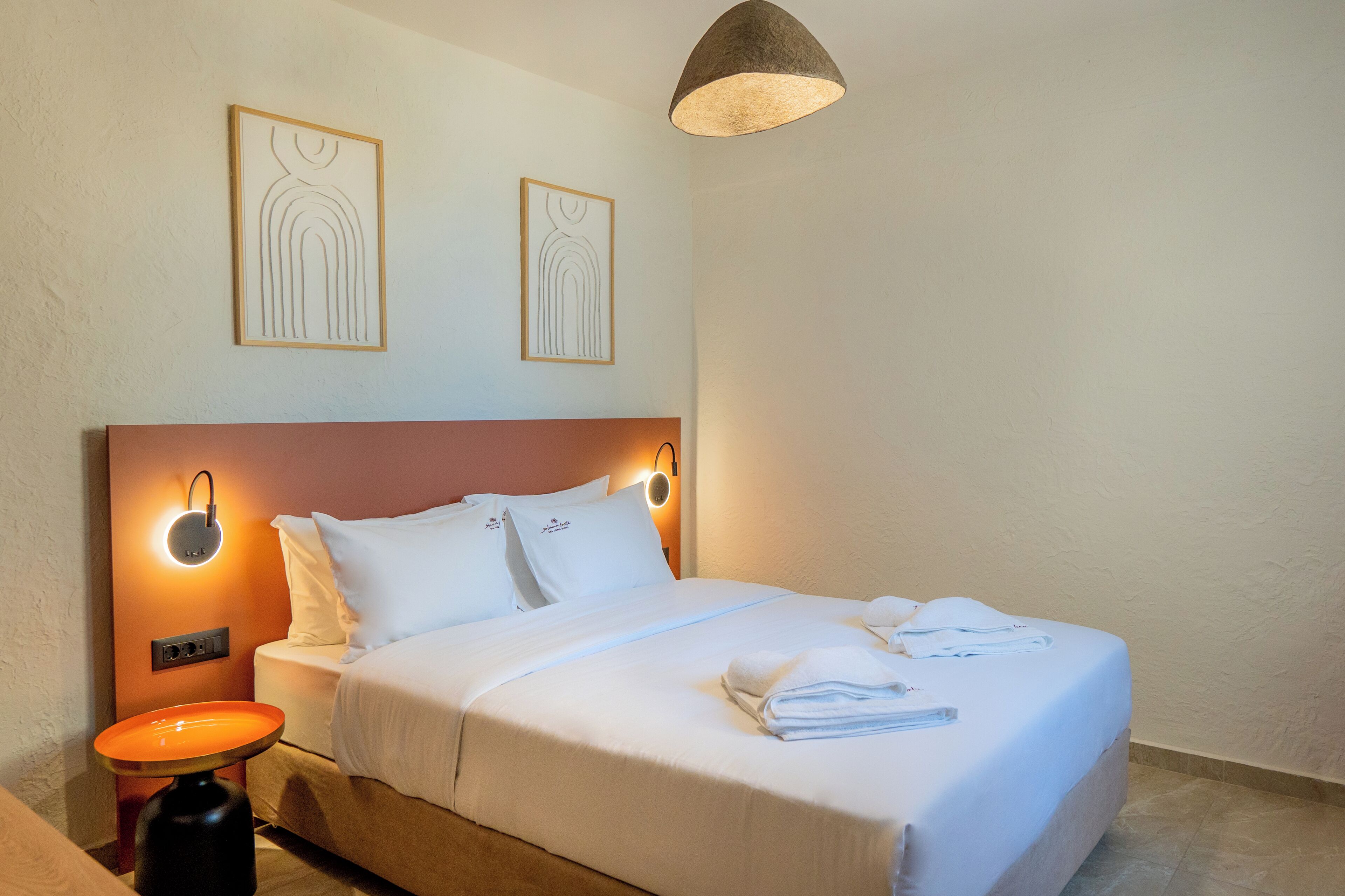 A neatly made bed with white linens, a bedside table with a lamp, and two wall-mounted light fixtures.
