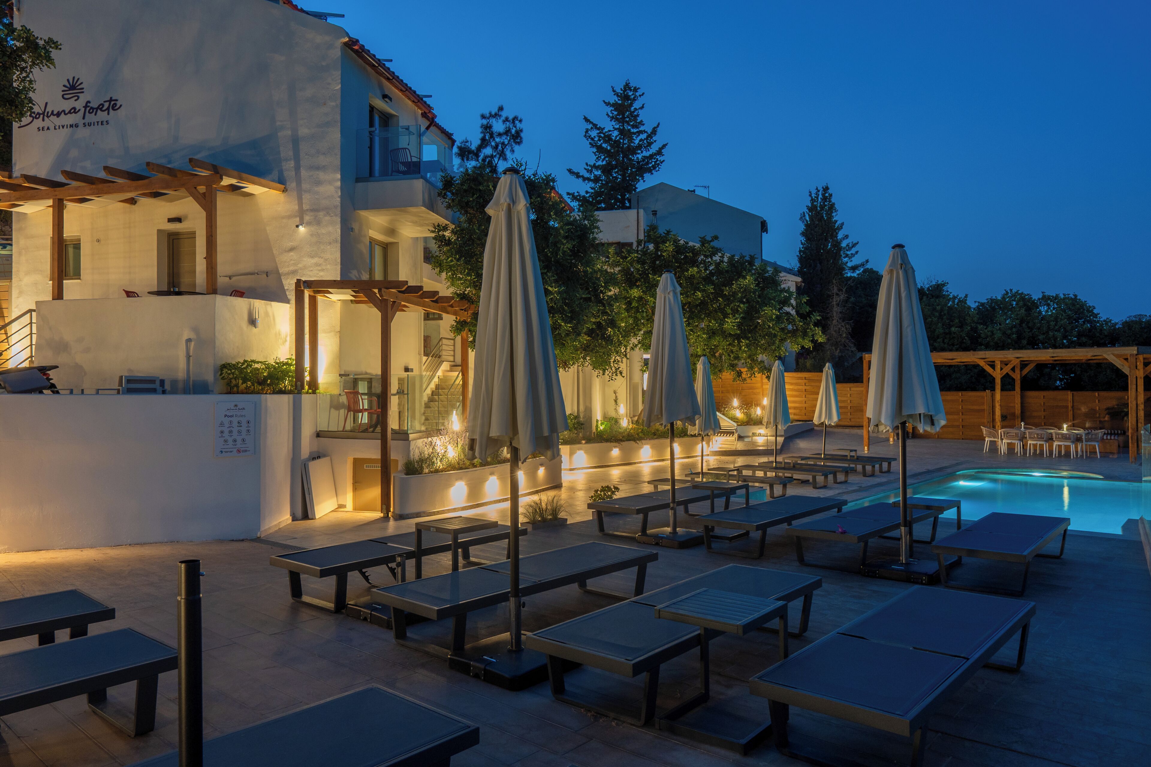A poolside area with lounge chairs and umbrellas, a pool, and a building with a sign reading 'Sea Living Suites'.