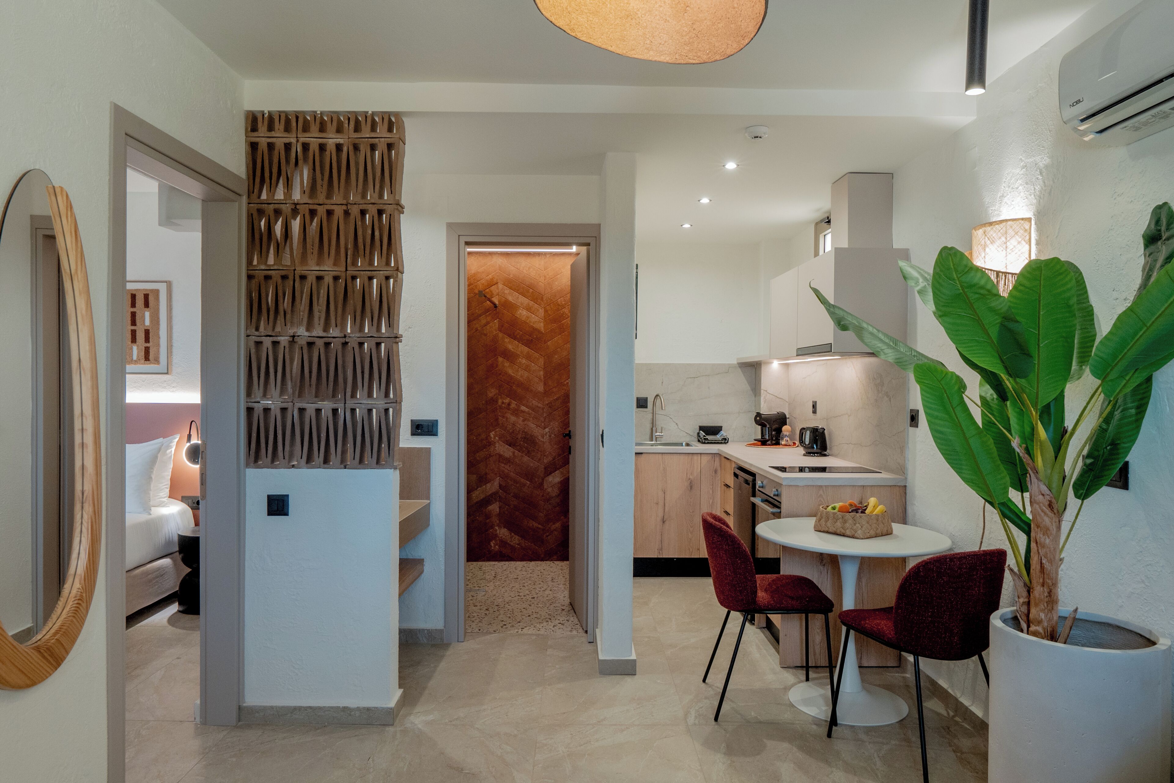 A modern kitchen with a herringbone-patterned backsplash, a dining area with two red chairs, and a large potted plant.