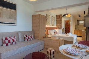 Une chambre d’hôtel moderne comprenant un canapé, un lit, une table à manger avec de l’assiette et des couverts, un meuble en bois et une œuvre d’art accrochée au mur.