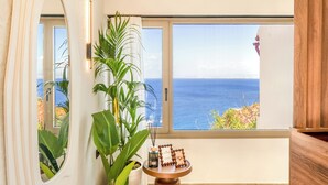 A room with a large window, a potted plant, a small table with decorative items, and a wooden cabinet. - Soluna Forte Sea Living Suites (Malevizi)