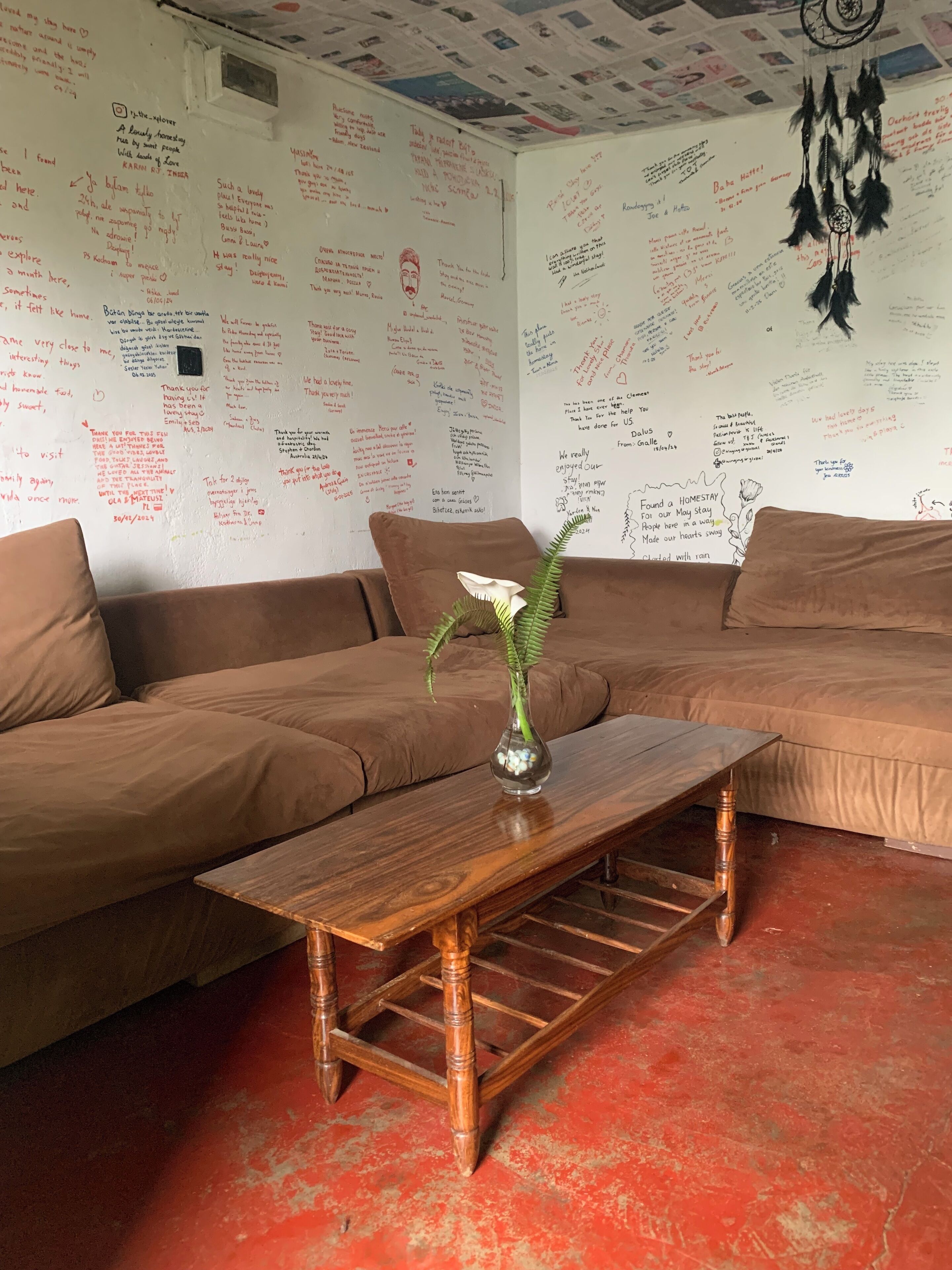 A cozy living room with a wooden coffee table, a vase with flowers, and a wall covered in handwritten notes.