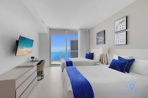A modern hotel room with two beds, a desk, and a large window offering a city view. - Hollywood Oceanfront Apt - 2BR (Hollywood)