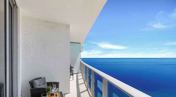 A balcony with wicker furniture and a table, overlooking a clear blue sea.