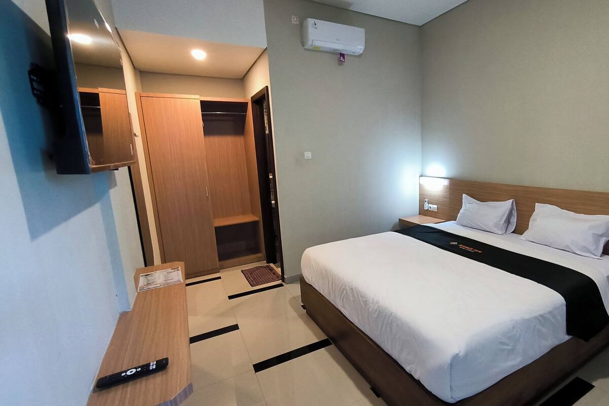 Una habitación de hotel con cama, mesita de noche, televisor, armario y aire acondicionado.