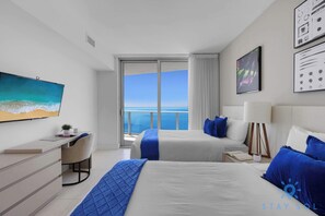 A modern hotel room with two beds, a desk, and a large window offering a view of the sea. - Hollywood 2BR Apartment w/Balcony (Hollywood)
