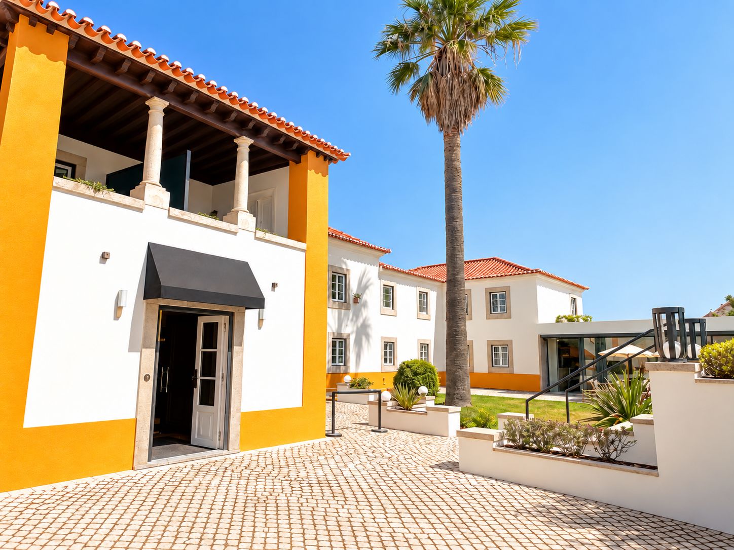 Um edifício com telhado de azulejos, uma palmeira e um acesso pavimentado.