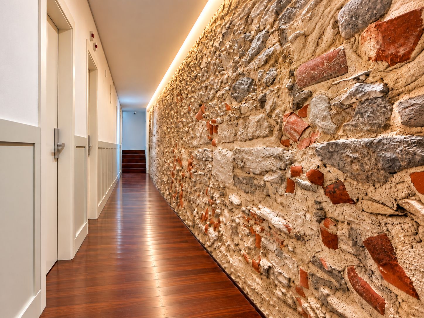 A hallway with a wooden floor and a textured wall with bricks and stones.