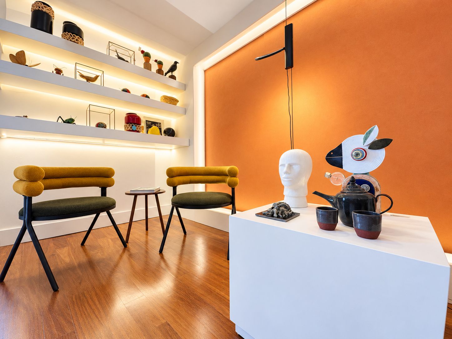 A modern interior with a white reception desk, two chairs, a small table, and a wall-mounted light fixture.