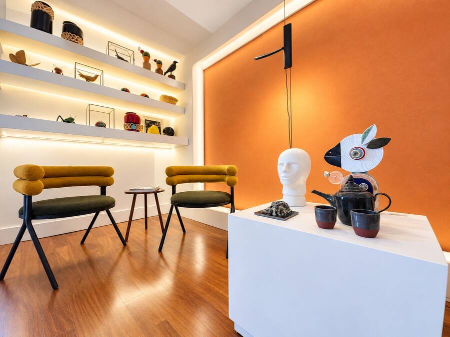 A modern interior with a white reception desk, two chairs, a small table, and a wall-mounted light fixture.